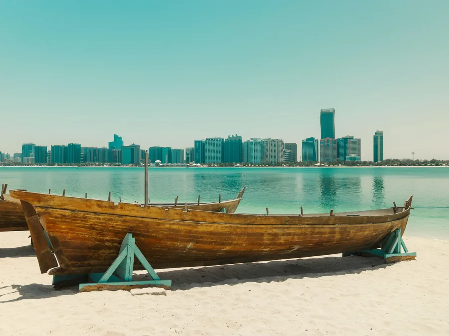 Wooden dhow on the beach with the Abu Dhabi skyline across the water